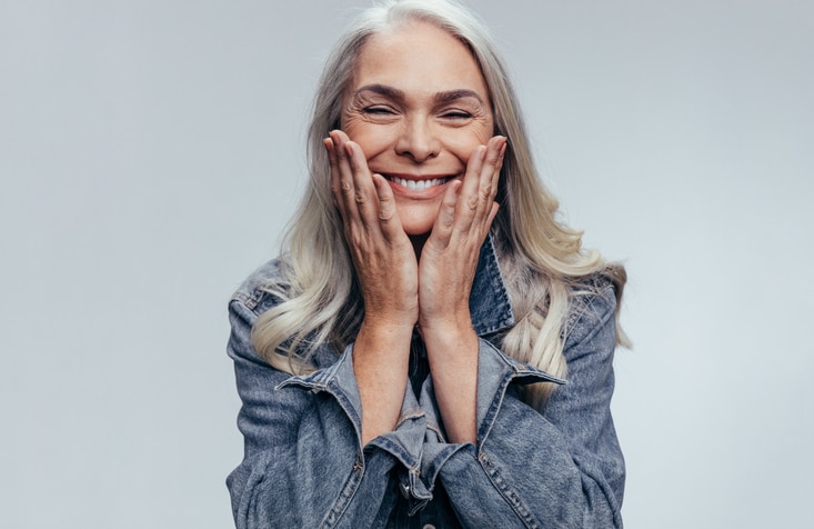 Older woman smiling with her hands on either side of her face.