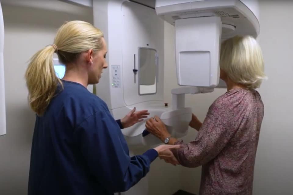 Dental assistant guiding a patient into an x-ray machine.