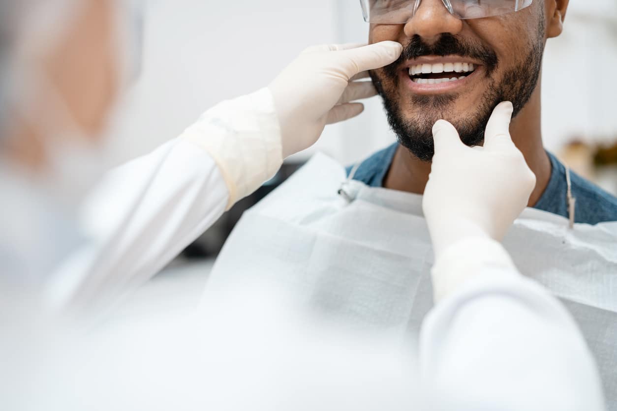 an orthodontist opening a male patients to inspect his teeth
