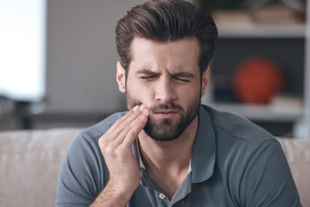 an adult male holding his cheek and a negative expression because of dental pain