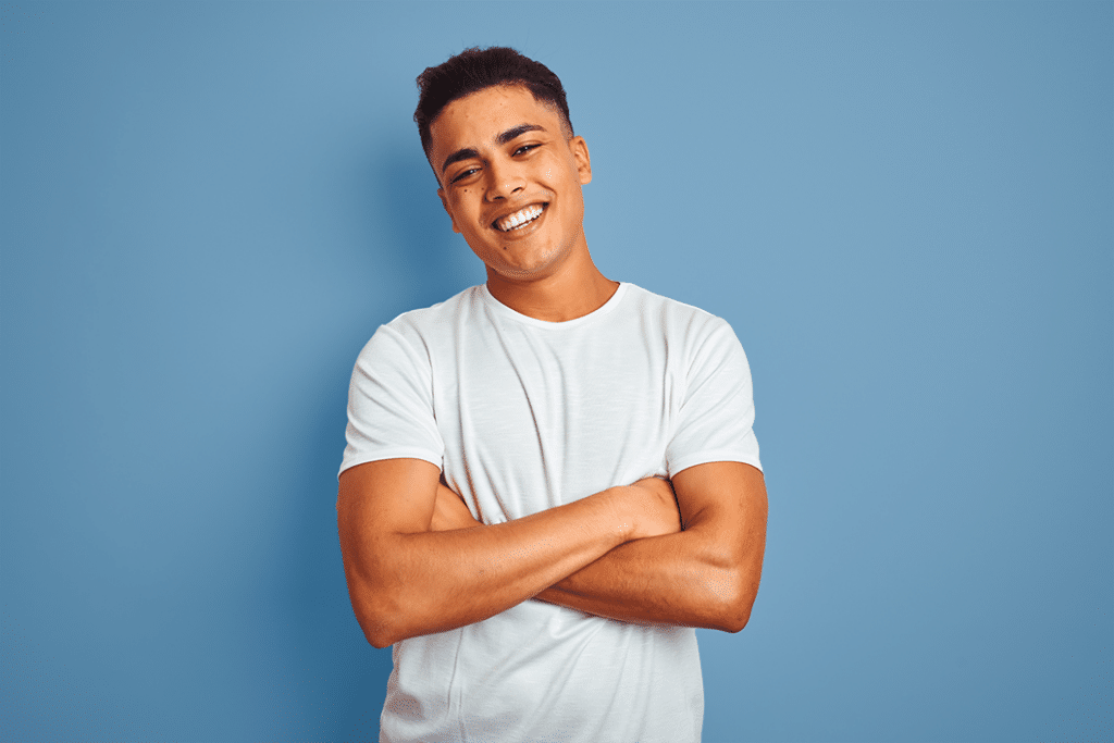 an orthodontic patient standing in front of a blue background with his arms crossed and a big smile