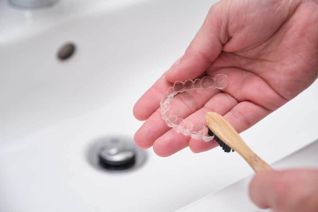 Image of someone cleaning a clear aligner tray with a toothbrush
