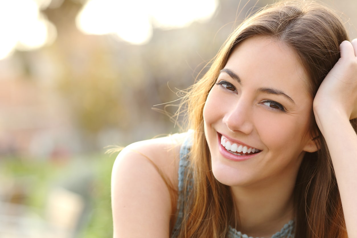 Young adult woman with great smile smiling at as sunlight illuminates her brown hair and shoulder