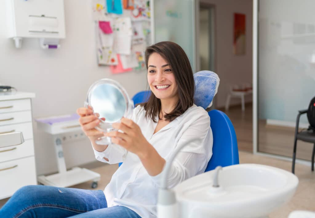 Woman examining her beaming smile in a dental chair at the end of an appointment