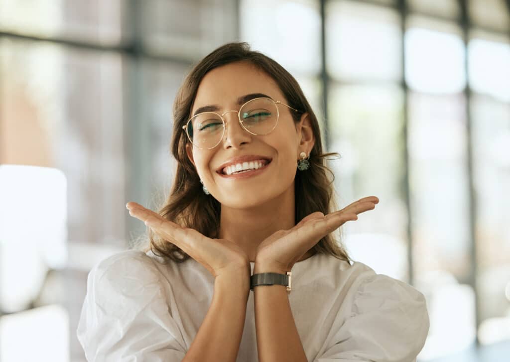 Woman with glasses posing with her hands under her face showing her smile