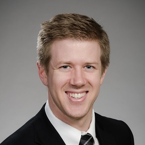 Matthew Carmody, DDS - Man smiling in a suit and tie against a grey background.