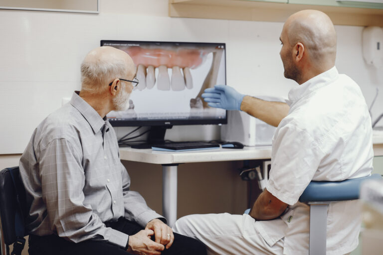 Dentist showing a dental diagram on a computer screen to an older patient in a dental office.