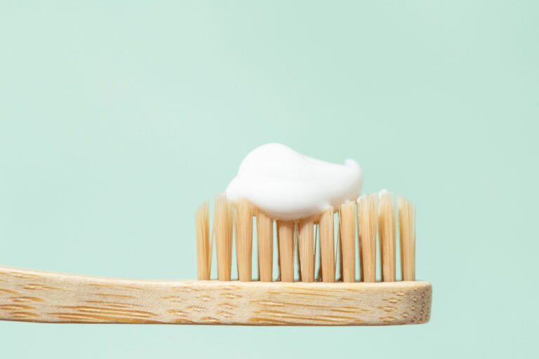 close-up image of a wooden toothbrush with white toothpaste on the bristles on a light green background