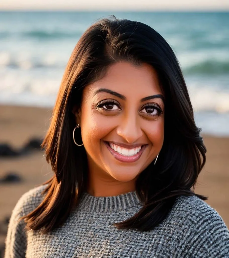 Headshot of Dr. Vanmali wearing gray sweatshirt and earrings, the background is beach.