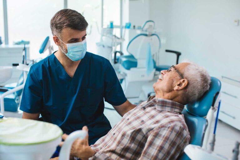 Dentist wearing a mask and gloves examining an elderly male patient in a dental chair