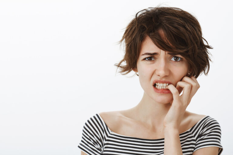 A woman with a chipped tooth nervously grasps her face.